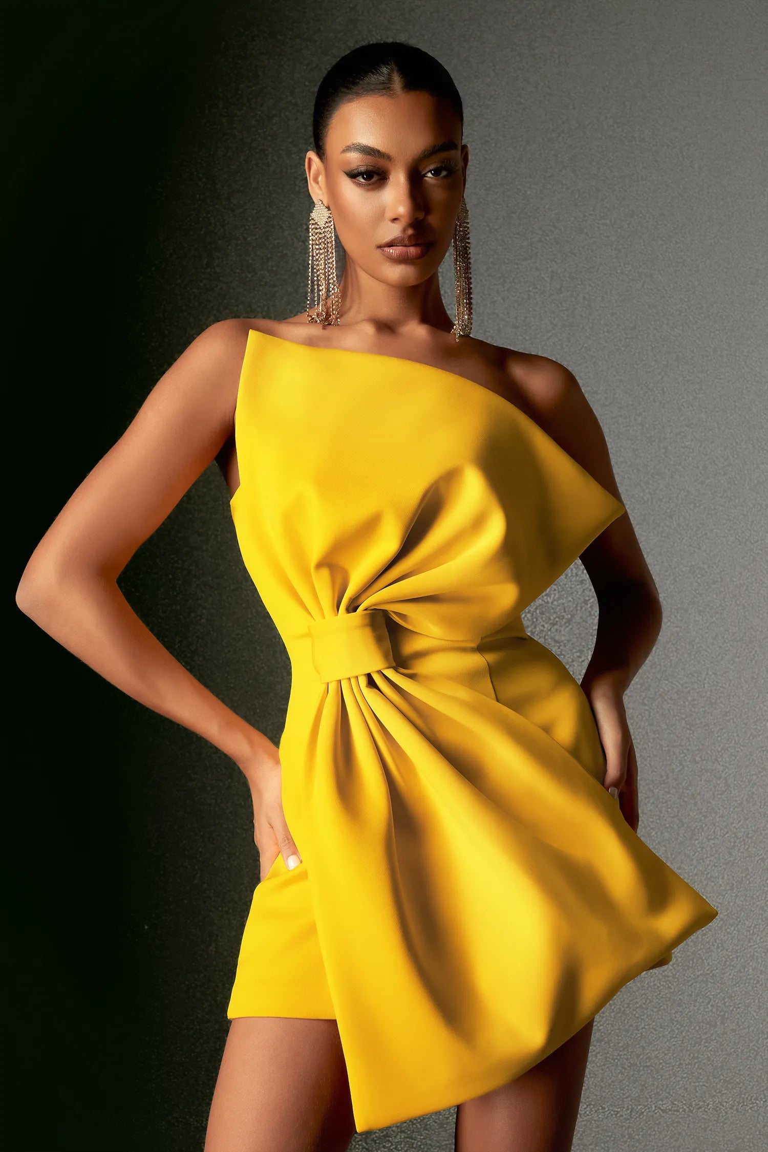A woman wearing a vibrant yellow strapless mini dress with an oversized bowknot detail at the front.