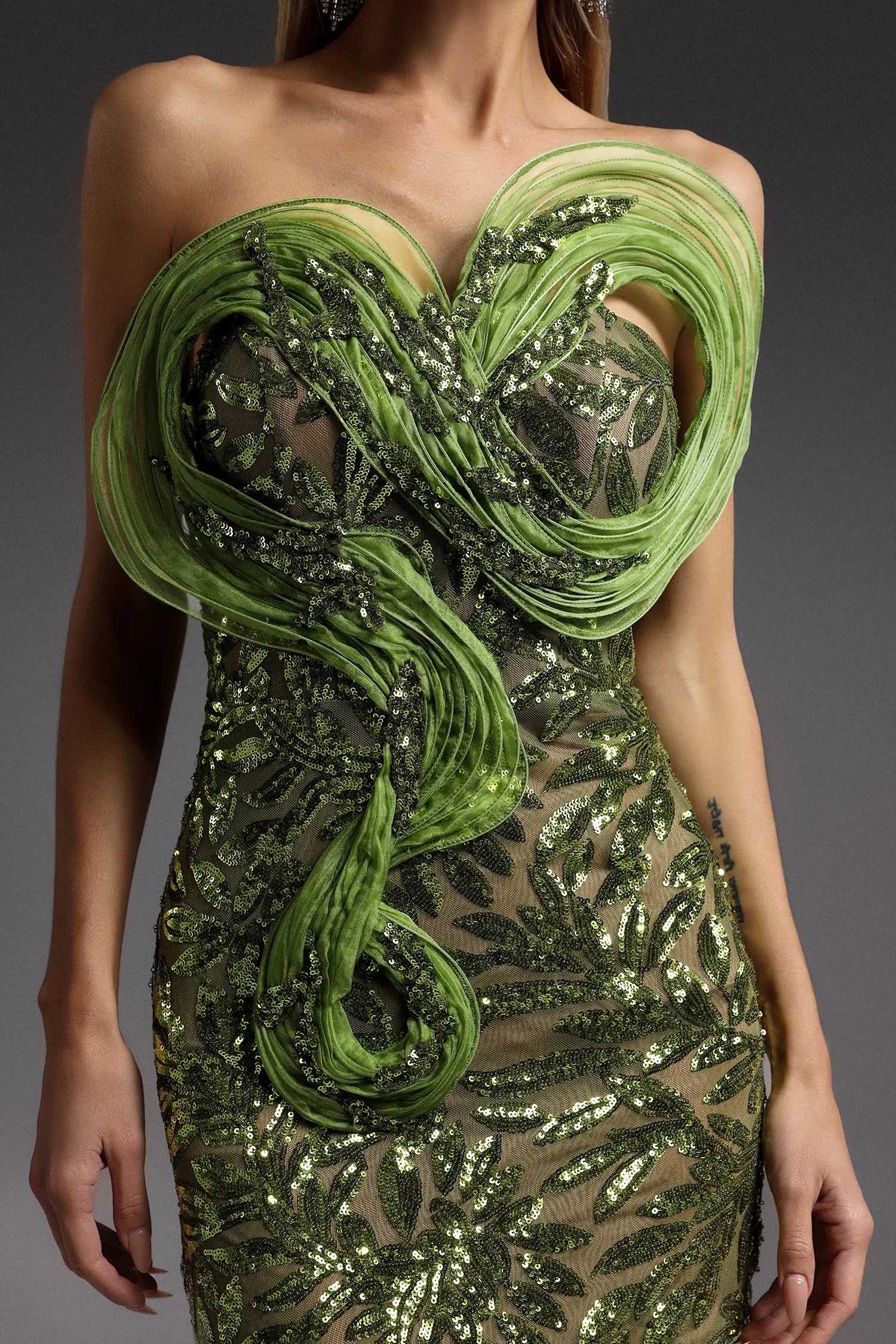 Model wearing green strapless mini dress with sequin embroidery and sculptural pleated fold detail